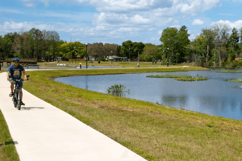 Tavares Ecological Park. A person rides a bike on the sidewalk beside a pond.